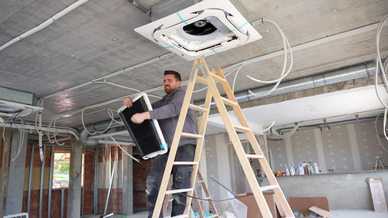 Man Installing Air Conditioner Unit on Ceiling at Construction Site