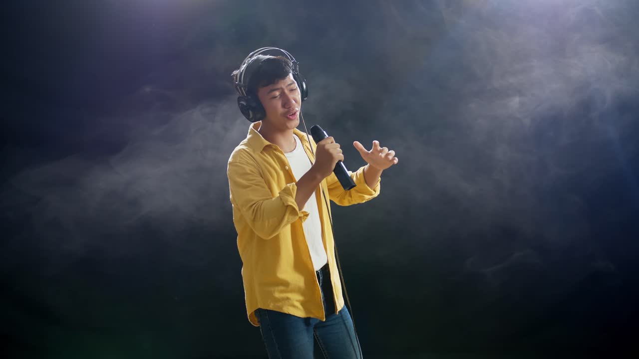 joven asiático con auriculares sosteniendo un micrófono y rapeando en el fondo blanco de humo negro