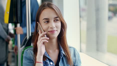 Cerca-De-La-Hermosa-Joven-Alegre-Sentada-En-El-Tranvía-Y-Hablando-Alegremente-En-El-Teléfono-Móvil-Mientras-Sonríe