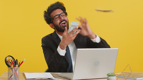Cheerful-rich-business-man-working-on-office-laptop-wasting-throwing-money-to-camera-profit-win