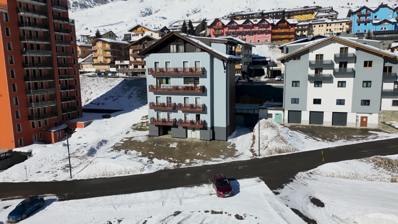edificio de hotel moderno cubierto de nieve con múltiples balcones en un entorno de montaña de invierno, vista aérea