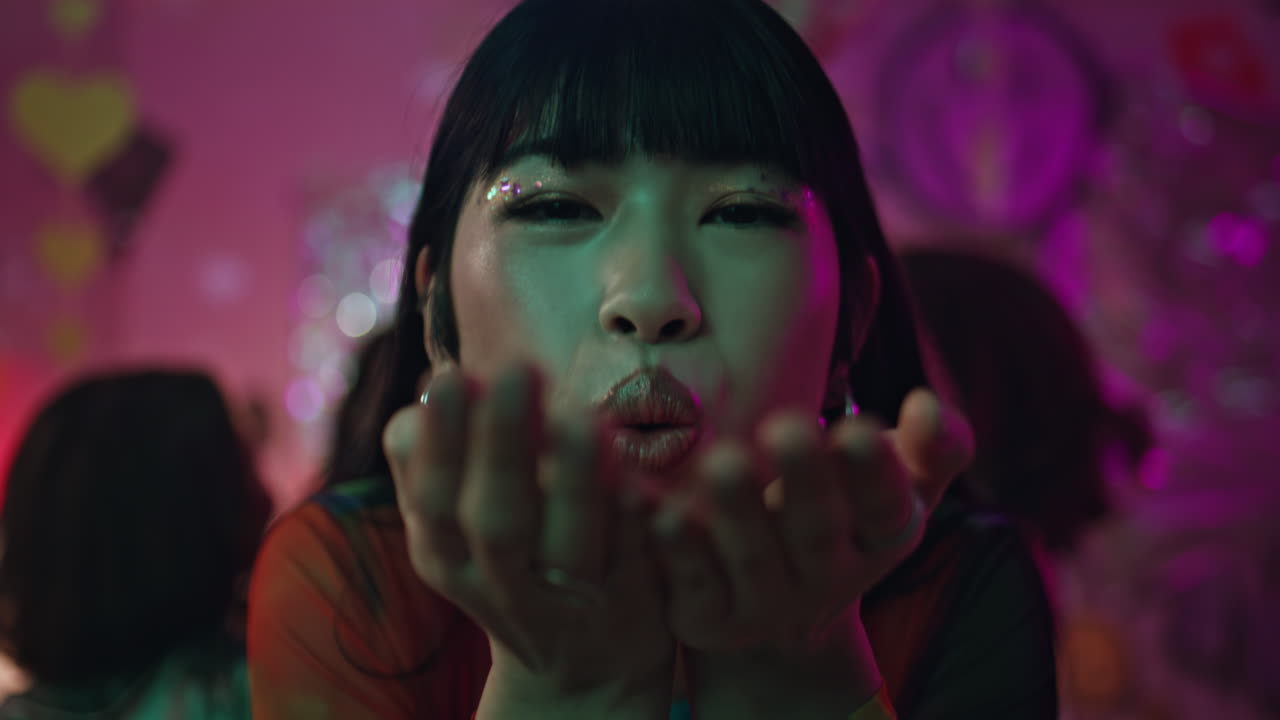 Smiling woman blowing confetti at neon party closeup. Happy girl dancing