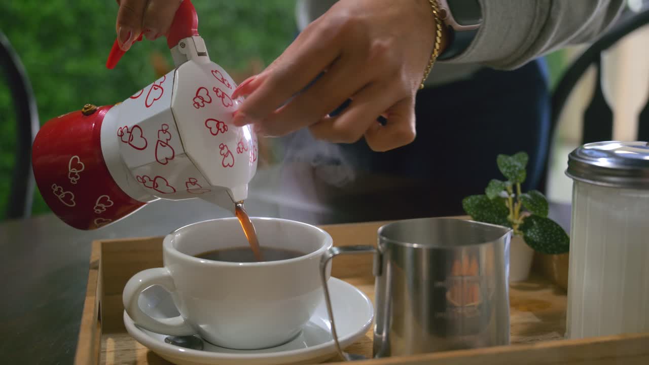 Un primo piano dettagliato di una persona che versa con cura una bevanda calda in una tazza bianca in una cucina luminosa e accogliente. Caffè