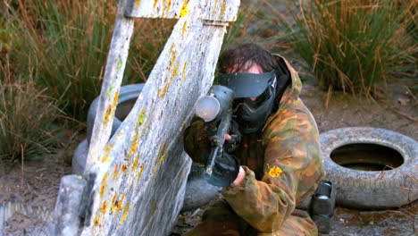 Man-crouching-behind-fence-shooting-paintball-gun