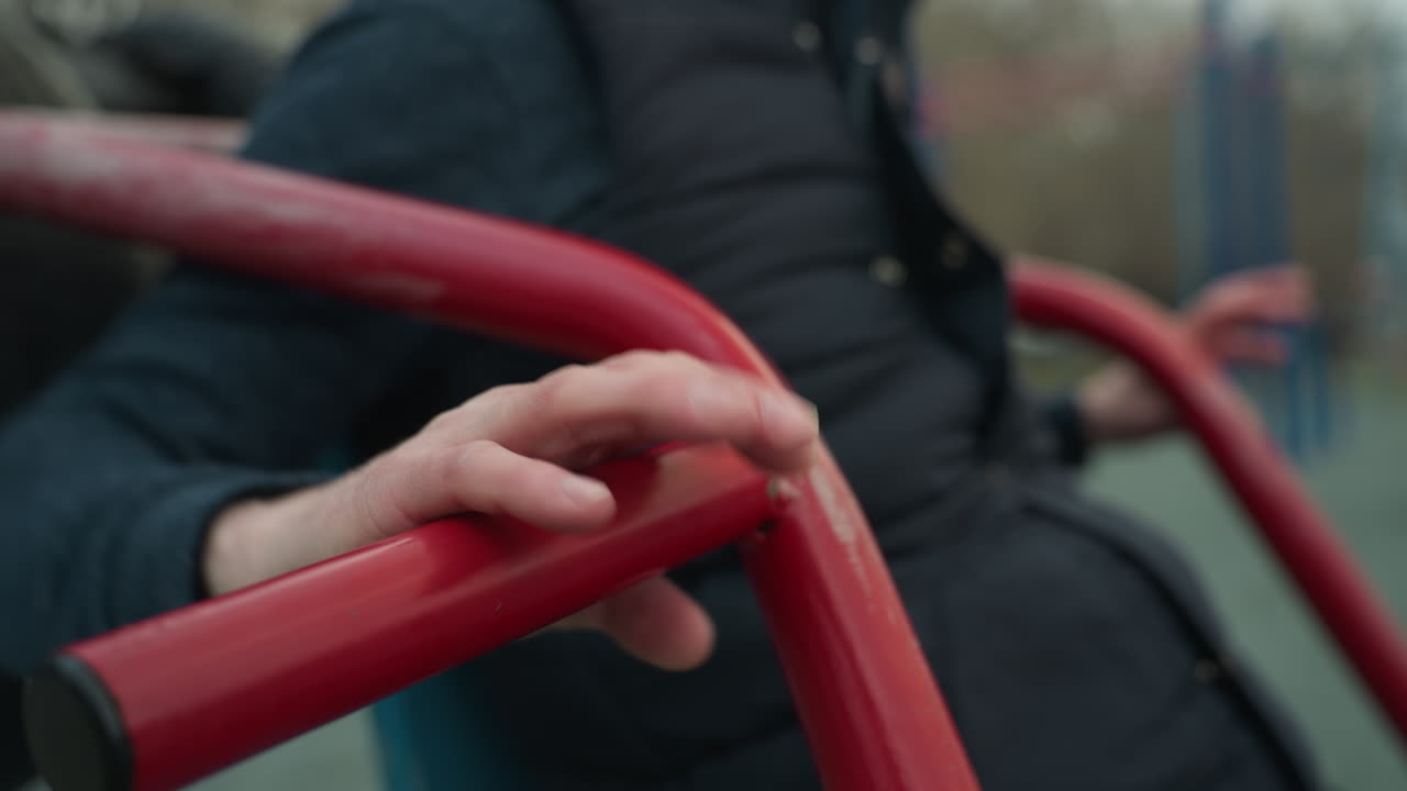 Close up of someone working out on a outdoor equipment, got tired after three pull-ups began to flex his hand on the iron, with blur view of someone in the background