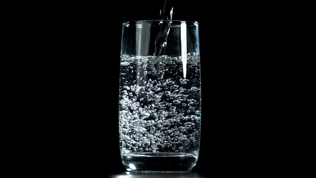 Acqua frizzante che si versa in un bicchiere trasparente con bollicine