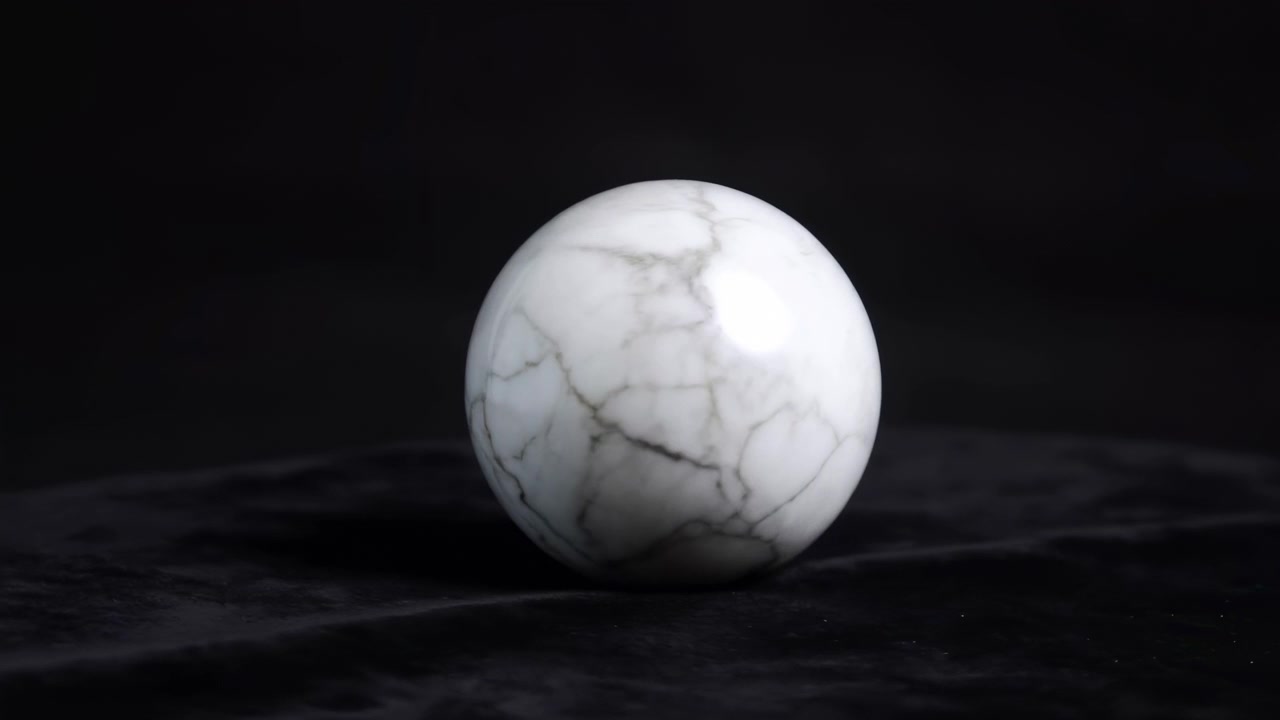 Primo piano a livello degli occhi basso di una sfera di marmo bianco lucido posizionata in basso al centro in primo piano su una superficie opaca scura con una profondità di campo ridotta.