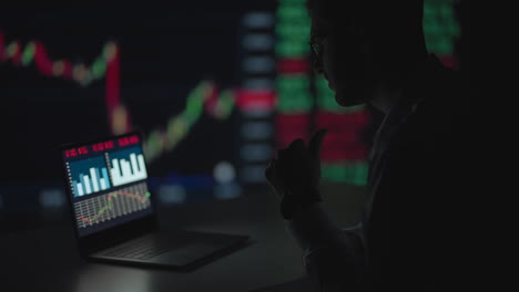 tarde en la noche en una oficina privada el hombre de negocios trabaja en una computadora portátil. tarde en la noche el comerciante lee números en sus múltiples pantallas con información de acciones en ellos