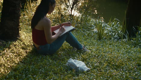 woman writing in a park by a lake at sunset