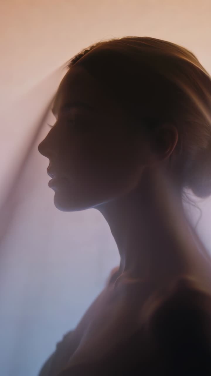 Vertical video: Veil drifting, strapless model lifting chin in studio catching backlight gradient
