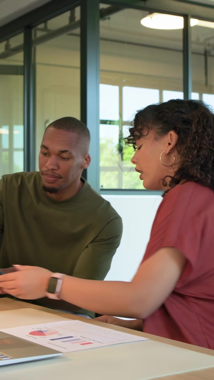 Vertical video: Woman at laptop checking charts, man coming with tablet starting business review