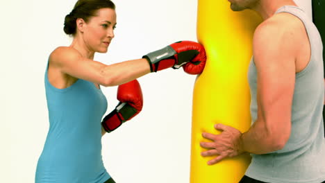 mujer en forma golpeando una bolsa sostenida por el entrenador