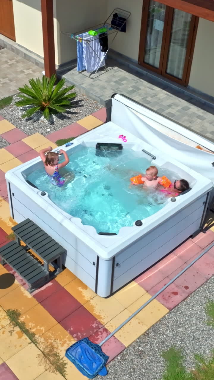 Vertical drone shot around a mommy and kids relaxing in a jacuzzi, sunny day