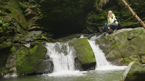 a woman in a yellow down jacket admiring the waterfall in the forest 4k video
