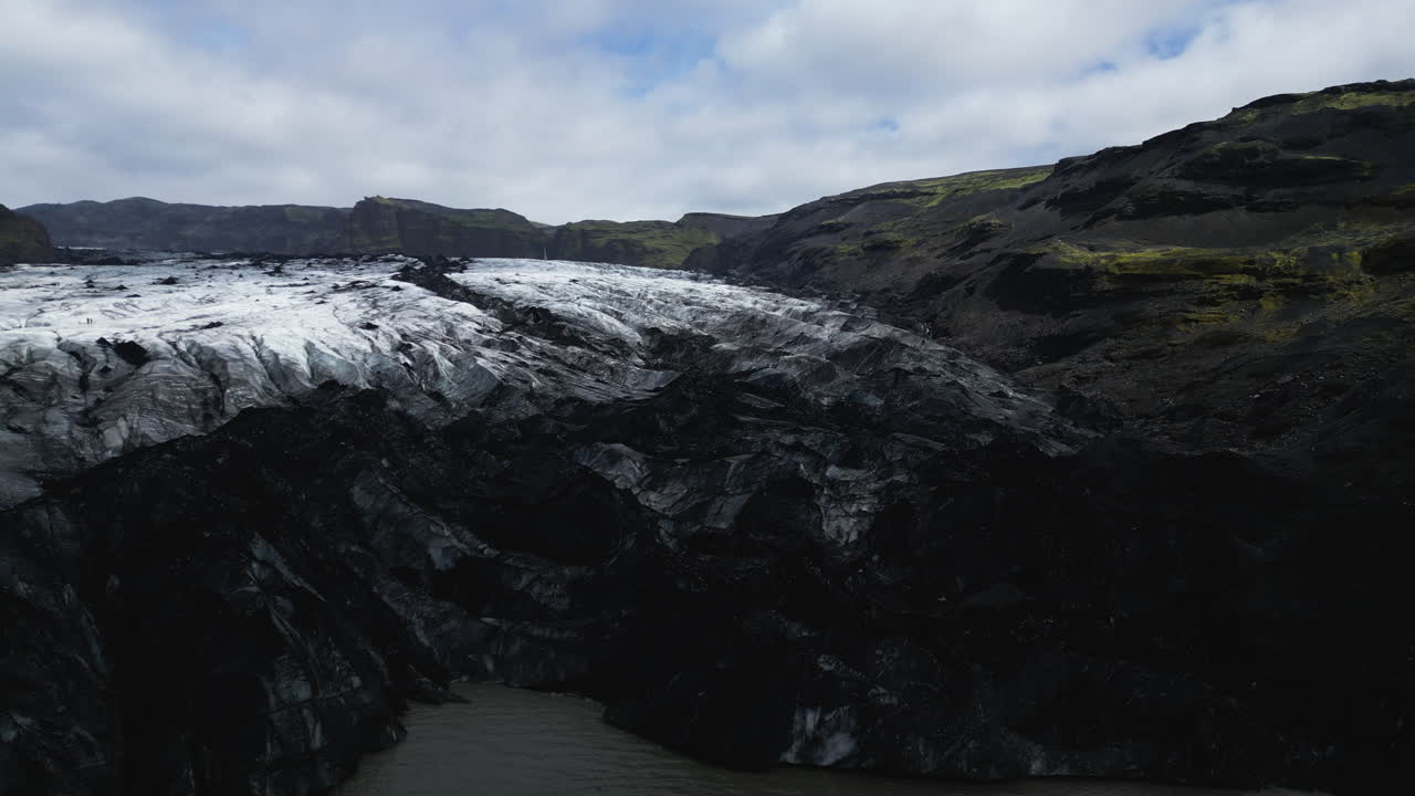 Snow covering black rocky glacier of Sólheimajökull glacier lake in Iceland. Aerial wide shot. Beautiful nature of Iceland