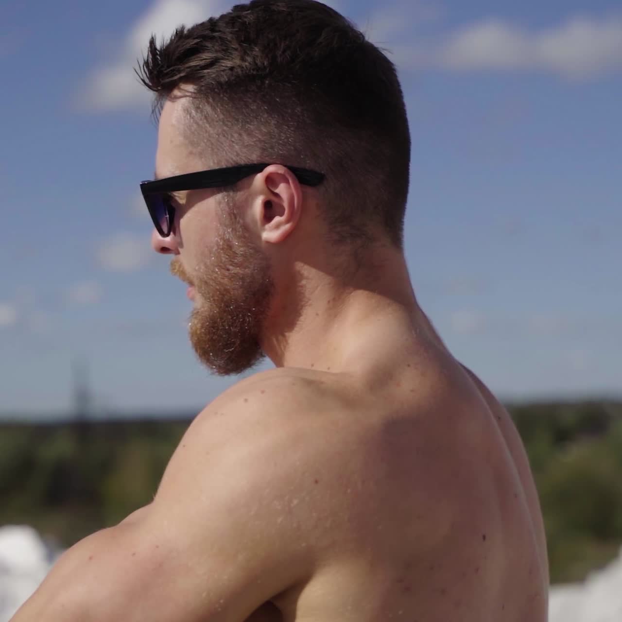Muscular athlete on the top of the hill. Face of a bearded guy in black sunglasses outdoors on the blur city background. Close-up.