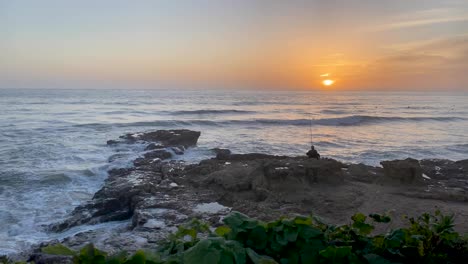 silhouette of a fisherman with a fishing rod at sunset over the sea