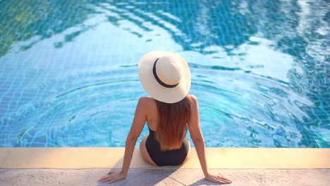 unrecognizable woman with sun hat sitting by the pool, high angle rear