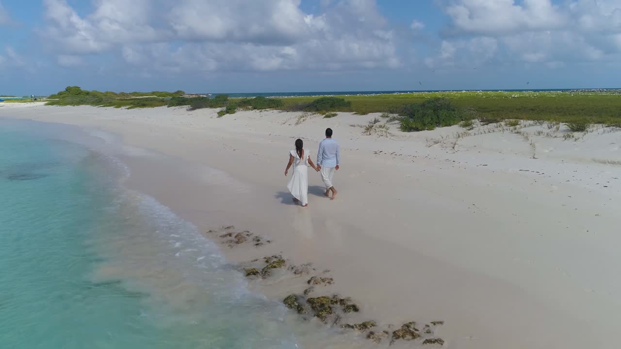 Koppel loopt hand in hand op zandstrand.
