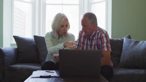 Senior-couple-with-laptop-using-calculator-and-checking-finances-while-sitting-on-the-couch-at-home