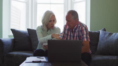 pareja de ancianos con computadora portátil usando calculadora y comprobando las finanzas mientras están sentados en el sofá en casa