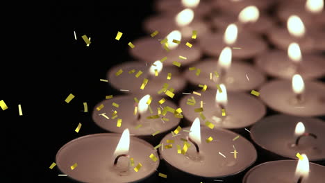 animation of gold confetti falling over lit tea light candles on black background