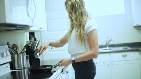 handheld slow motion shot of a young blonde female cooking chicken in a pan over a stove