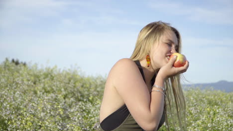 slomo of young woman eating an apple in a field of flowers