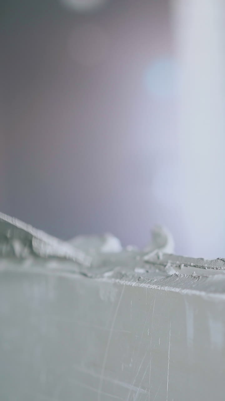 professional painter arm in special gloves holds putty knife and smears gypsum plasterboard wall with primer closeup