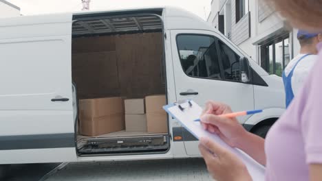 two young workers of removal company unload boxes and furniture from minibus into customer's home