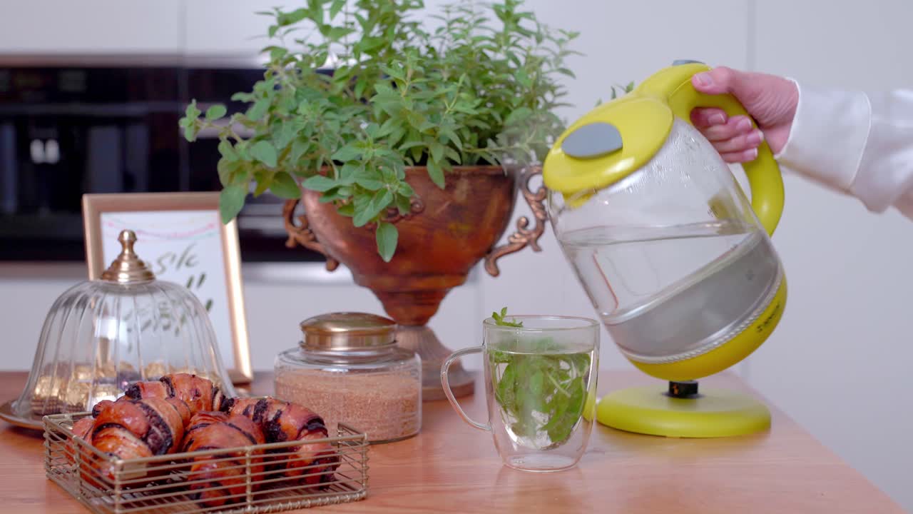 Tabletop electric kettle, hand pouring boiled water into glass with tea leaves