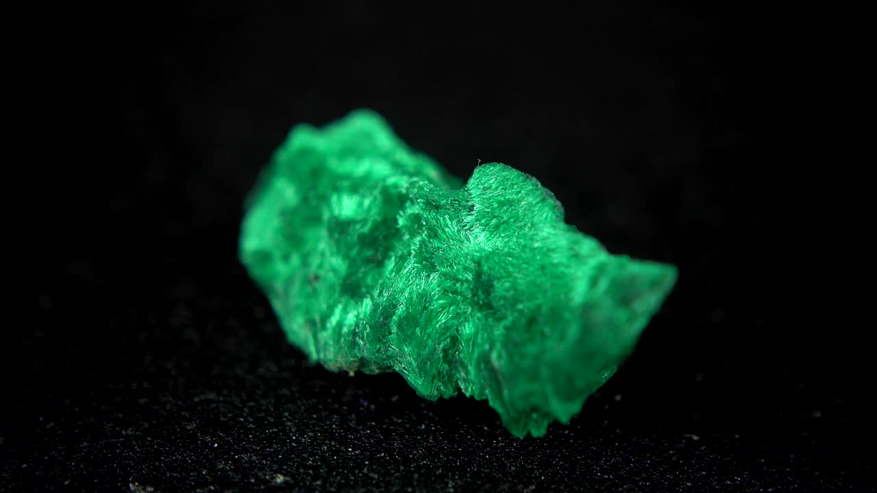 검은색 배경 앞에 녹색 광물 (말라카이트) 을 원활하게 회전시니다.