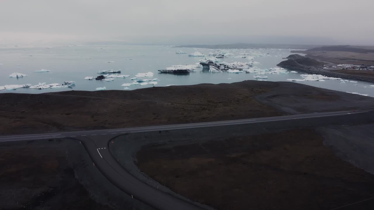 una foto de drones de hermosos icebergs blancos y negros flotando en una laguna en islandia aparecen detrás de playas de arena negra y la carretera de circunvalación