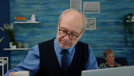 Close-up-of-senior-man-writing-at-laptop-working-from-home