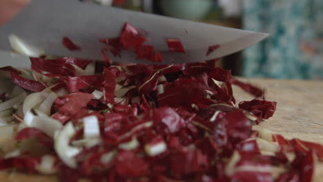 Close-up-woman's-hand-gently-chopping-Italian-chicory-with-a-sharp-knife-on-a-wooden-board-in-her-kitchen