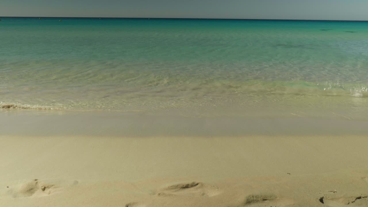 Levende blå havbølger slår ind over en uberørt hvid sandstrand og skaber en beroligende, naturlig kystscene.
