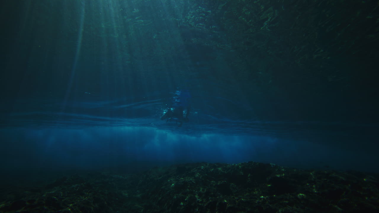 пана через риф к серферу утка ныряет, чтобы избежать мощной волны, когда светлые лучи сияют и текстурированный вихрь волны растет