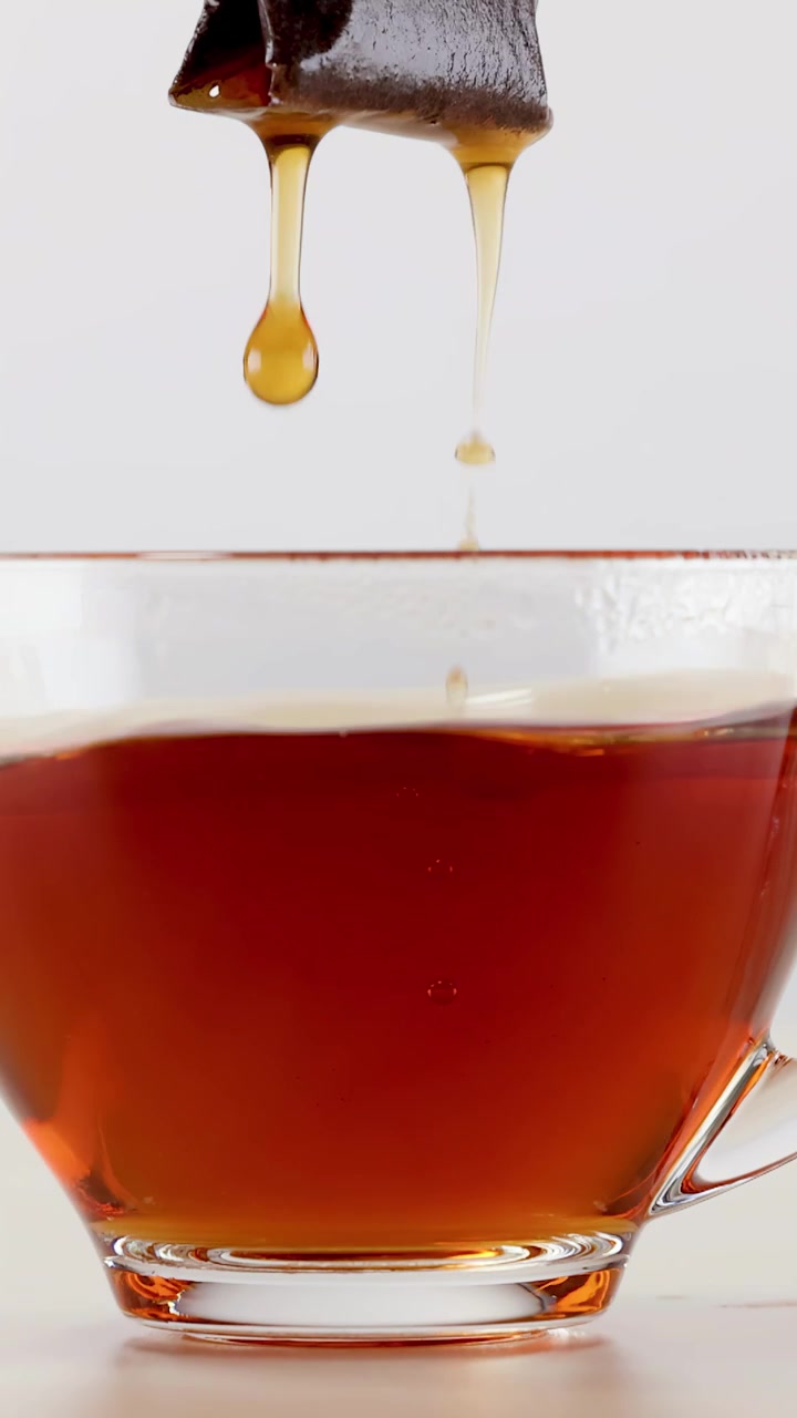 Primo piano di una bustina di tè che si immerge in una tazza di vetro trasparente di tè nero in infusione.