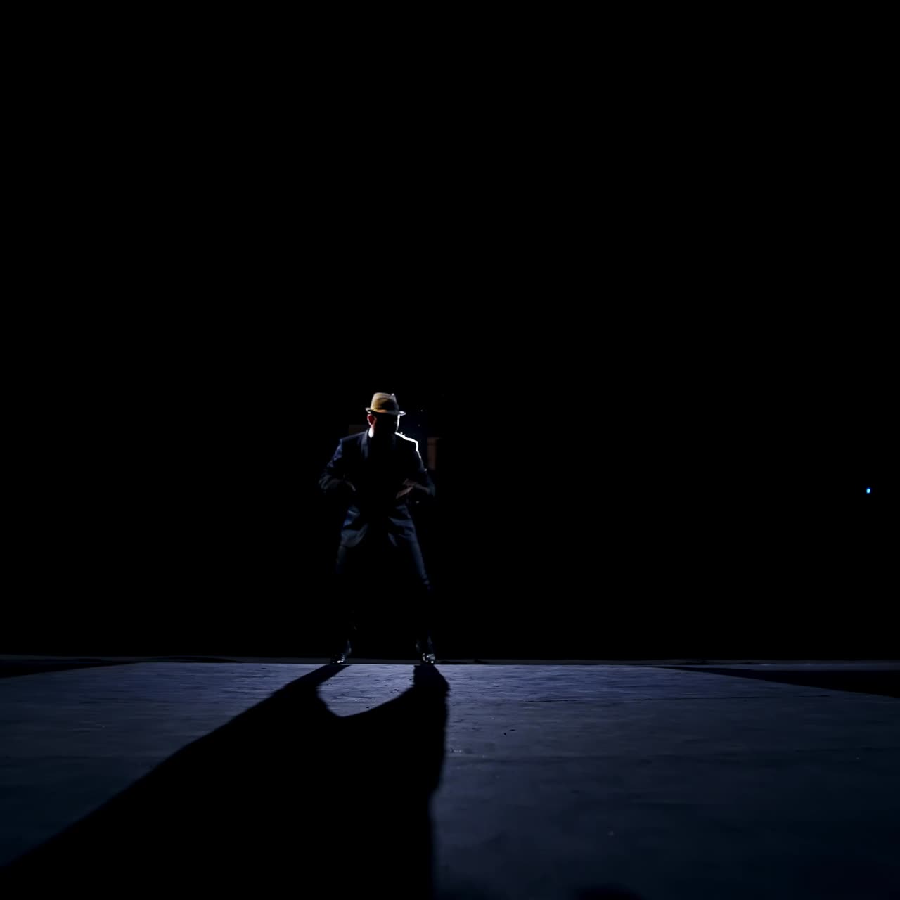 Silhouette of a dancer in move. Performer dancing on stage against spotlights on dark background. Man acting in the theater