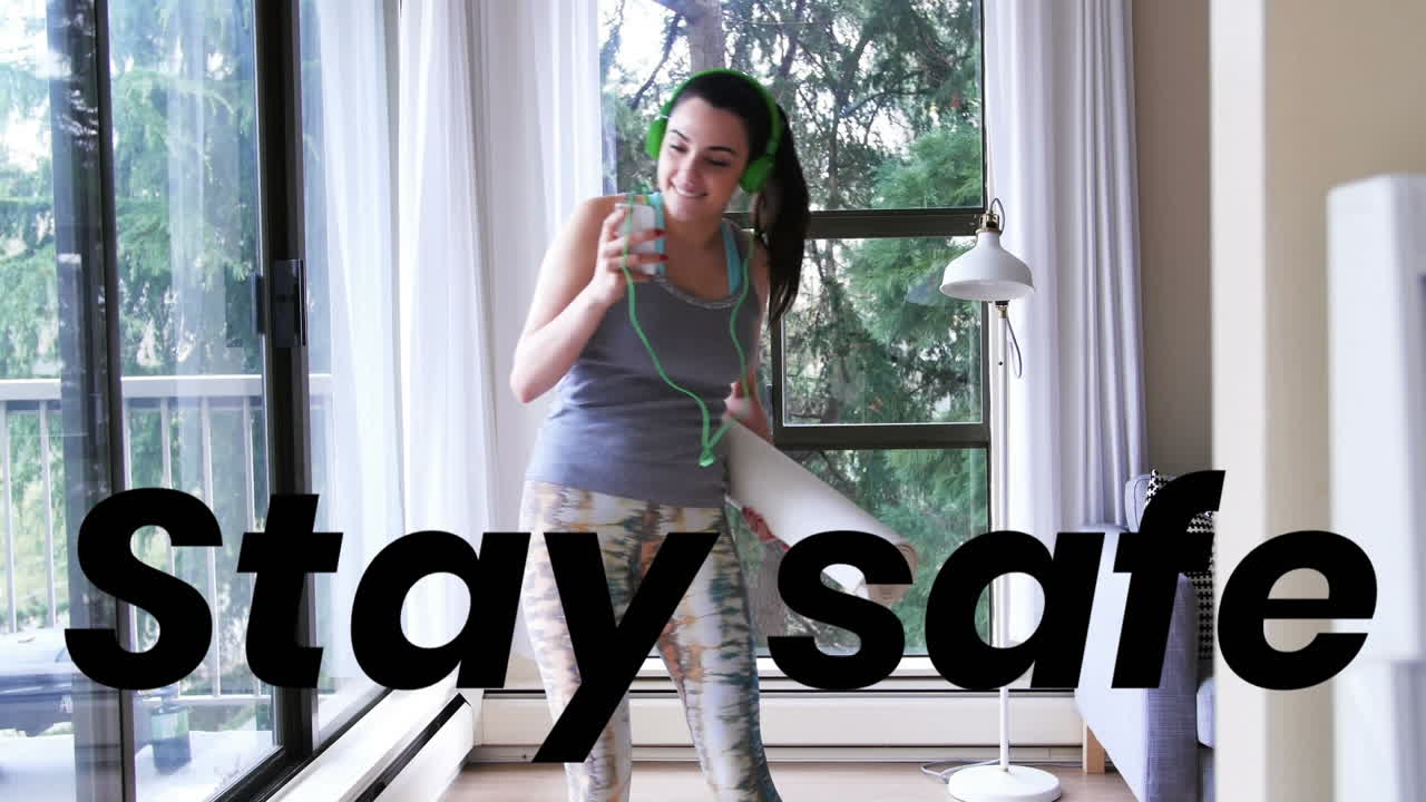 Animation of stay safe text over woman using smartphone holding yoga mat at home