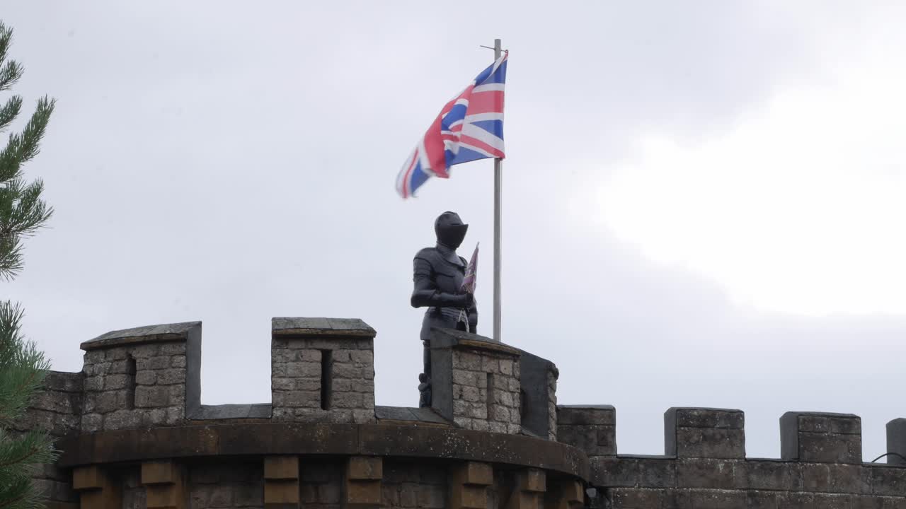 A British knight protecting a castle with the union jack flag fling on a pole.
