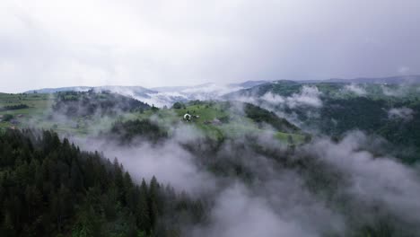 Aerial-orbit-view-of-village-on-top-of-green-forest-hill-on-a-misty-morning,-Transylvania,-Romania