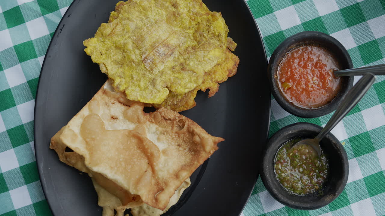 Questo primo piano cattura la consistenza croccante di ojaldre e tostadas colombiane, servite con salse vivaci su una tovaglia a quadri. Perfetto per rappresentare scene culinarie culturali.