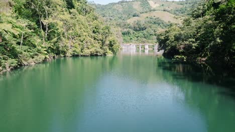 aerial approaching shot of green river with dam of tireo during sunny day, dominican republic