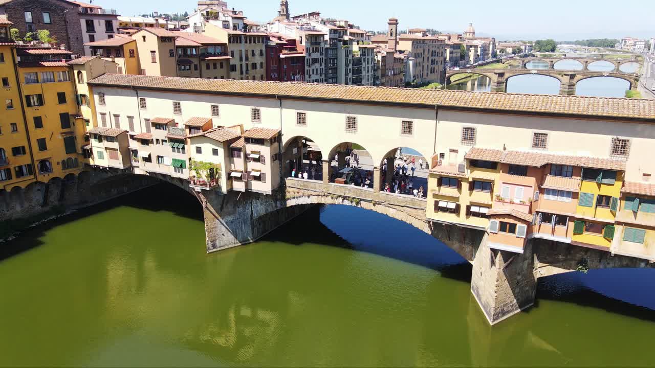Vibrant Historic Ponte Vecchio, tourists above emerald water in Florence, Italy