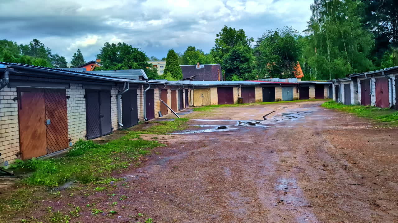 Row of Old Garage Units With Puddles and Overgrown Grass in Suburb