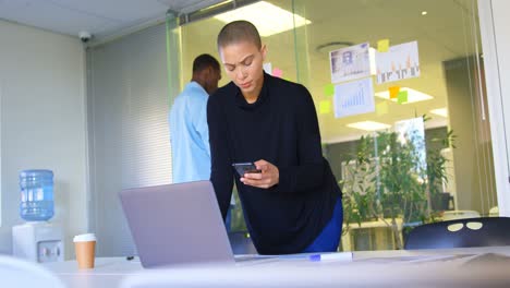 Front-view-of-young-caucasian-female-executive-using-mobile-phone-while-working-on-laptop-in-modern-