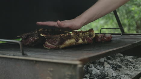 Red-meat-steaks-and-sausages-roasting-on-grill-as-man-checks-heat-with-his-hand