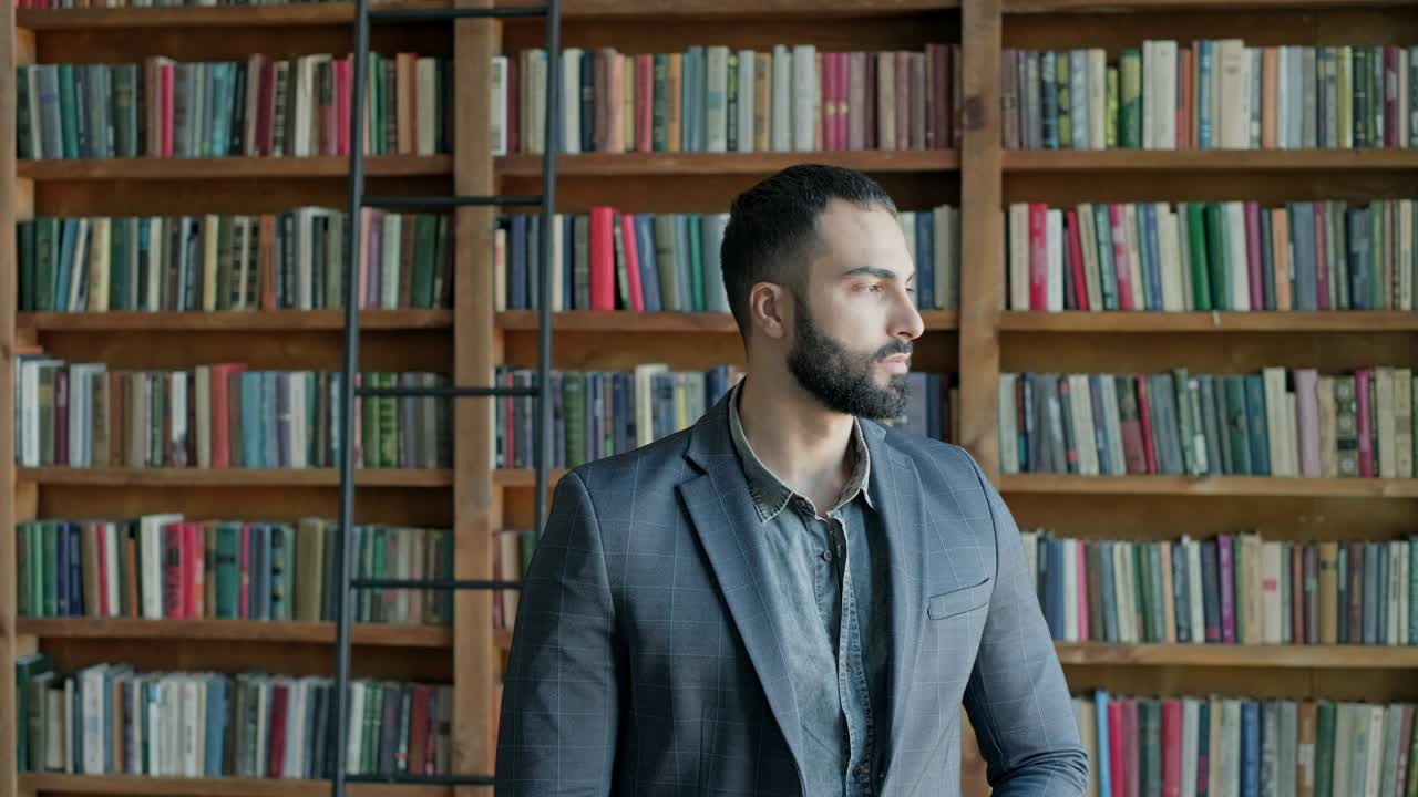 un tipo está de pie en la biblioteca. una morena atractiva con barba de oriente medio.