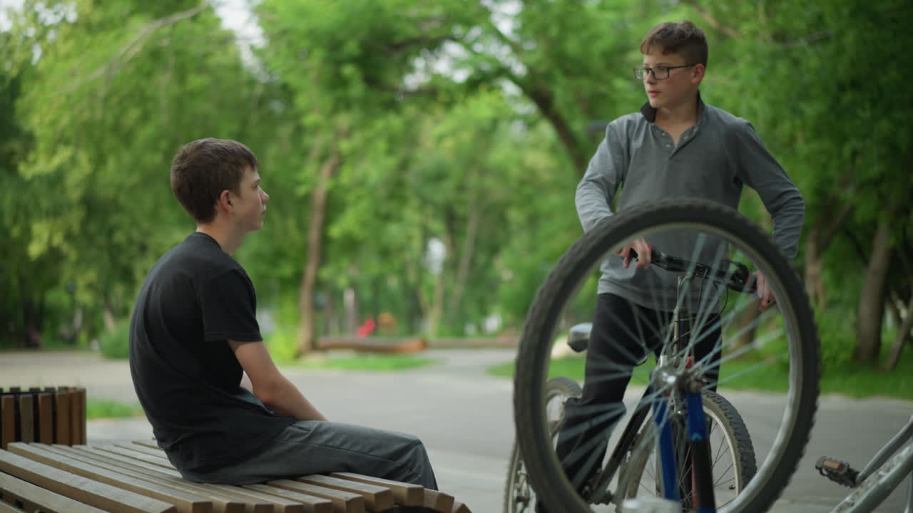 자전거를 타고 자전거 에 앉아있는 어린 소년은 바 바 자전거와 함께 다른 소년이 접근합니다. 그들은 평화로운 공원에서 초록색으로 둘러싸인 대화에 참여합니다.